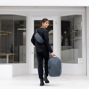Person wearing a Thule sling bag and carrying a Thule backpack outside a shop