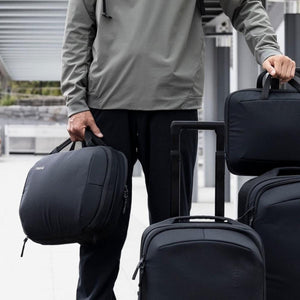 Person holding multiple black Thule travel bags and luggage