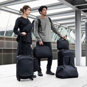 Man and woman standing with various Thule black luggage pieces and backpacks