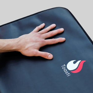 Hand resting on a black ToastiMat surface with a flame logo
