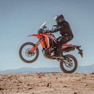 Rider on a Honda CRF300L Rally motorcycle jumping over a desert hill