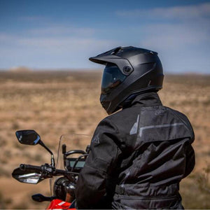 Motorcyclist wearing a black adventure helmet and jacket on a motorcycle in a desert landscape