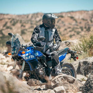 Rider wearing Tourmaster jacket and helmet on a blue Yamaha motorcycle in a rocky desert landscape