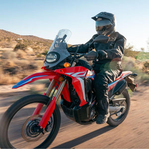 Motorcyclist wearing Tourmaster gear riding a red dual sport motorcycle on a dirt road