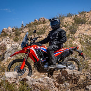 Rider wearing Tourmaster jacket and pants on a red Honda motorcycle in a rocky desert landscape