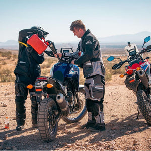 Two motorcyclists in Tourmaster gear refueling a motorcycle in the desert