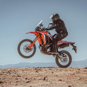 Rider wearing Tourmaster gear on a Honda motorcycle jumping over a desert hill