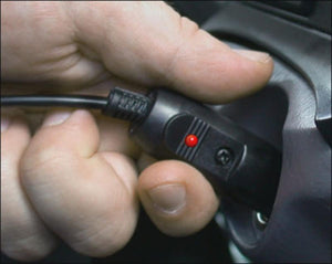 Trillium Worldwide car power adapter with red indicator light being plugged into a vehicle socket