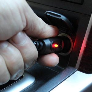 Hand inserting a car charger adapter into a vehicle power outlet with a glowing red indicator light