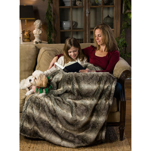 Woman and child reading a book on a sofa under a faux fur throw blanket with a small dog