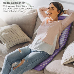 Woman sitting on a sofa using a purple UTK Technology heating pad against her back