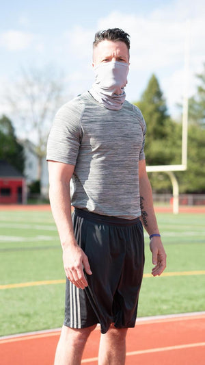 Man wearing a grey neck gaiter and athletic clothing standing on a running track