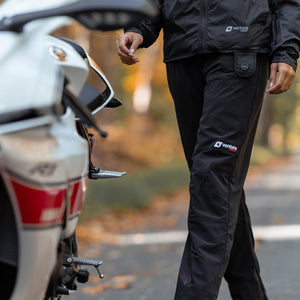 Person wearing Venture Heat black heated pants standing next to a motorcycle