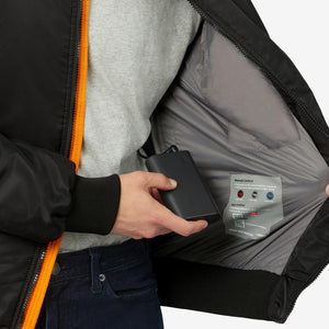 Person holding a Venture Heat power bank inside the inner pocket of a black heated jacket