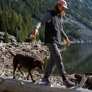 Man wearing Venture Heat vest walking on a log with a brown dog by a lake