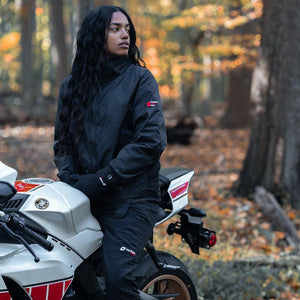 Person wearing Venture Heat black jacket and pants sitting on a white motorcycle in a forest