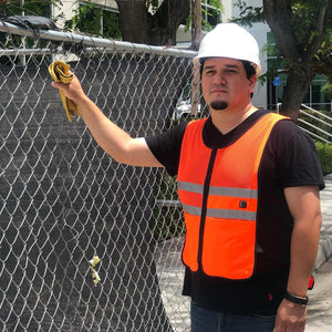 Worker wearing a Venture Heat orange safety vest and white hard hat standing by a chain link fence