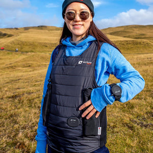 Person wearing a black Venture Heat heated vest over a blue hoodie in a grassy field