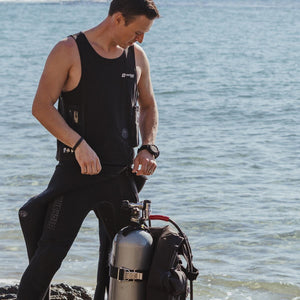 Man wearing Venture Heat vest and wetsuit standing by scuba tank on beach