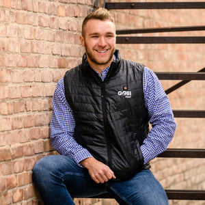 Man wearing a black Gobi Heat quilted vest over a blue gingham shirt