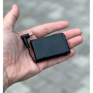Small black rectangular battery pack with a short power cable and connector held in a palm