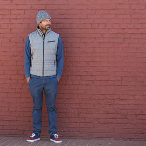 Man wearing a grey vest and beanie standing against a red brick wall