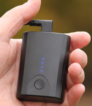 Hand holding a small black portable battery pack with four blue LED indicator lights and a power button