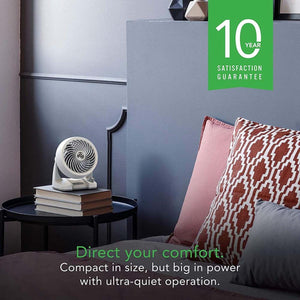 White Vornado air circulator fan on a stack of books next to a bed with a 10 year satisfaction guarantee graphic