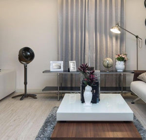 Vornado pedestal fan in a living room with a white coffee table and grey curtains