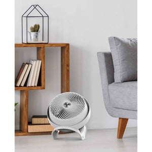 White Vornado air circulator fan on a floor next to a wooden shelf and sofa