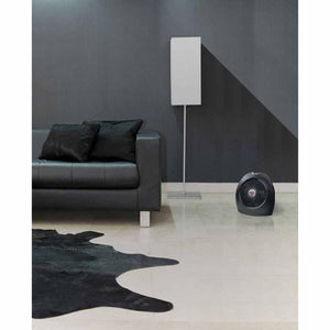 Black Vornado heater on a light floor next to a black leather sofa