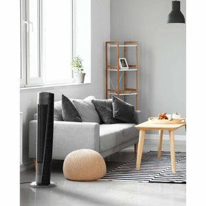 Vornado tower fan standing in a living room next to a grey sofa