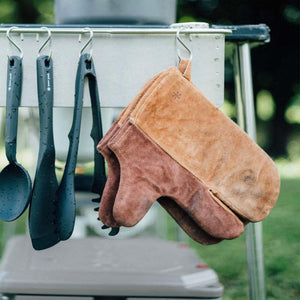 Snow Peak suede oven mitts and black cooking utensils hanging on a metal rack