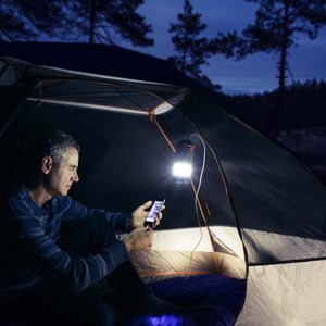 Man charging a smartphone with a Wagan lantern inside a tent at night