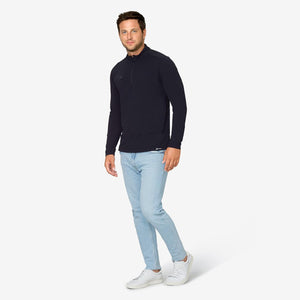 Man wearing a navy long sleeve quarter zip pullover with light blue jeans and white sneakers