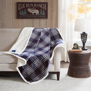 Woolrich navy and white plaid heated throw blanket with sherpa lining draped over a sofa