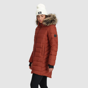 Woman wearing an Outdoor Research rust colored puffer parka with a faux fur hood and white beanie