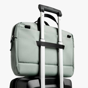 Sage green laptop bag attached to the handle of a black rolling suitcase