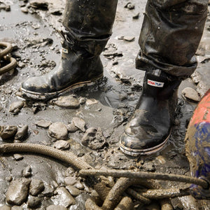Person wearing muddy Xtratuf boots standing on wet rocky ground