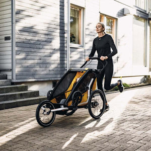 Woman jogging on a paved path pushing a yellow and black Thule child carrier