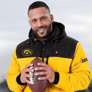 Man wearing a black and yellow Iowa Hawkeyes jacket holding a football
