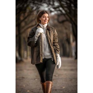 Woman wearing a brown wax jacket over a fleece with white mittens and brown leather boots walking on a path
