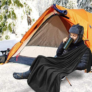 Person in winter gear using a Zone Tech black fleece blanket while sitting in a chair outside a tent in the snow